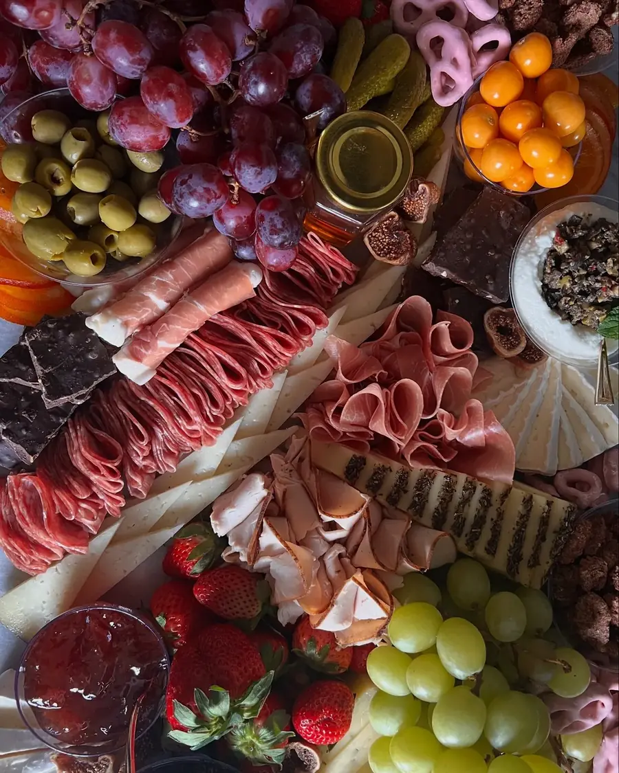 Board of grapes, olives, salami and dried citrus arranged in tight rows