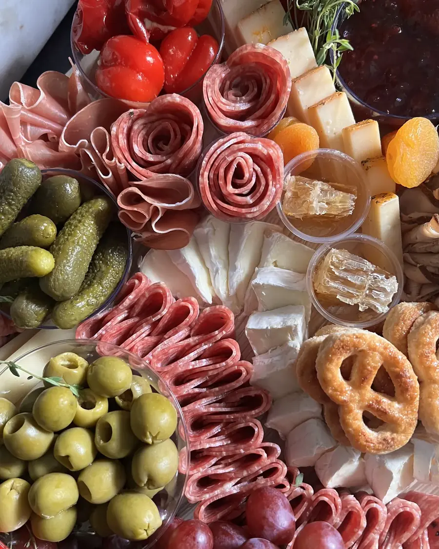 Overhead view of cured meat rosettes, olives, pretzels and marinated vegetables
