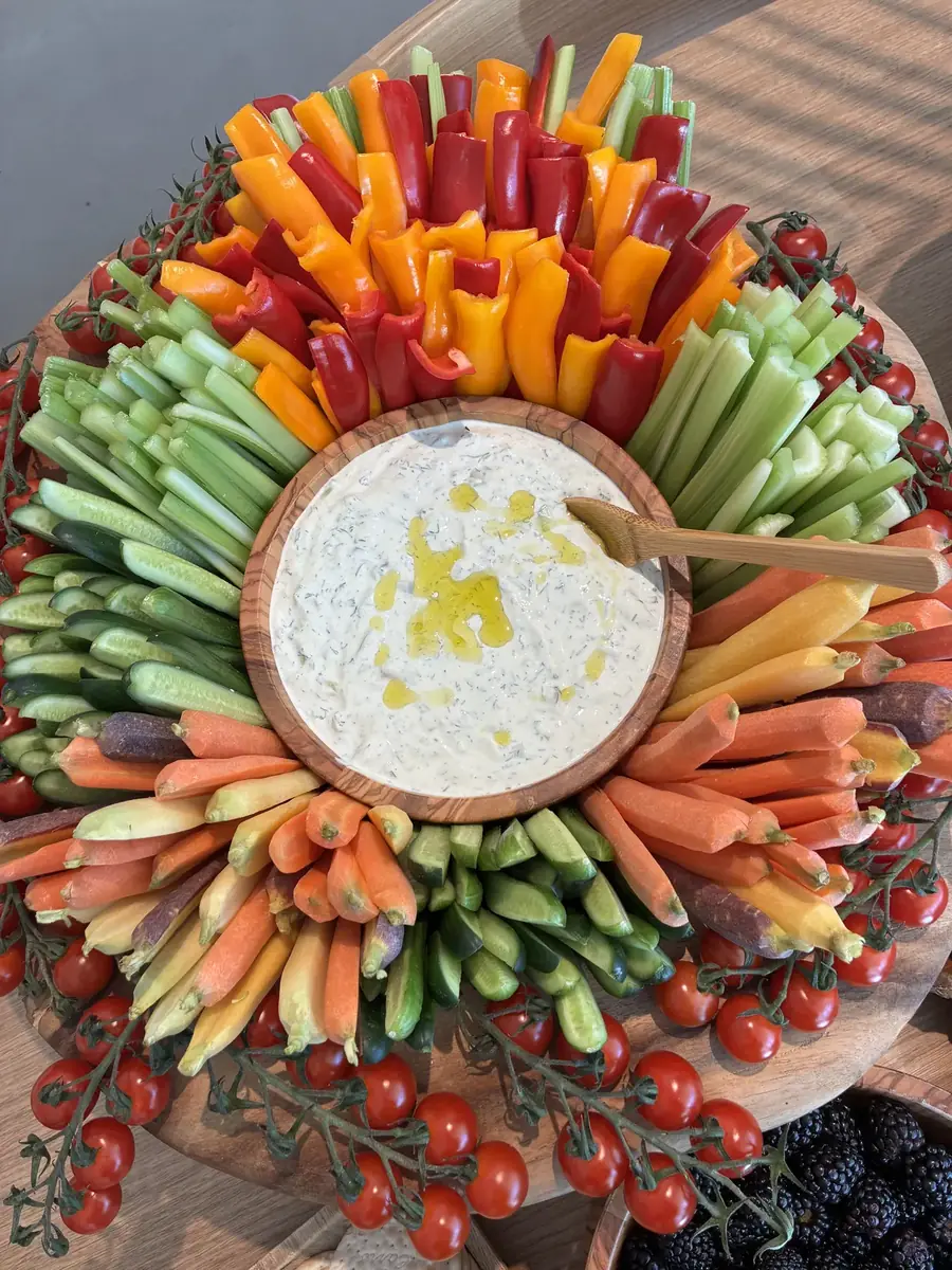 Circular crudite wreath of peppers, carrots and tomatoes ringing a bowl of dip