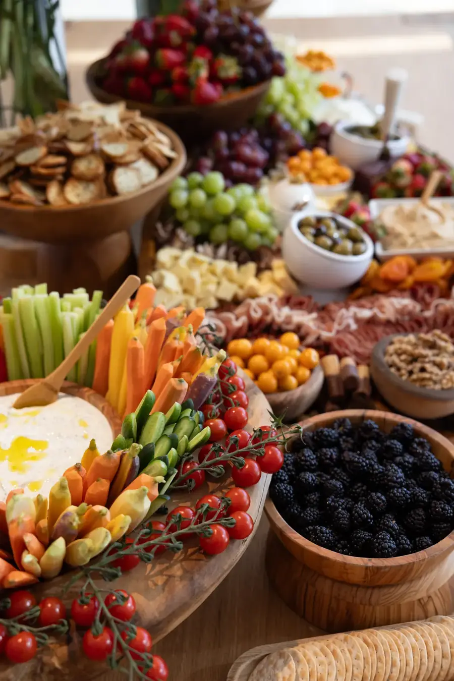 Grazing table layered with crudites, berries, nuts and crackers in wooden bowls