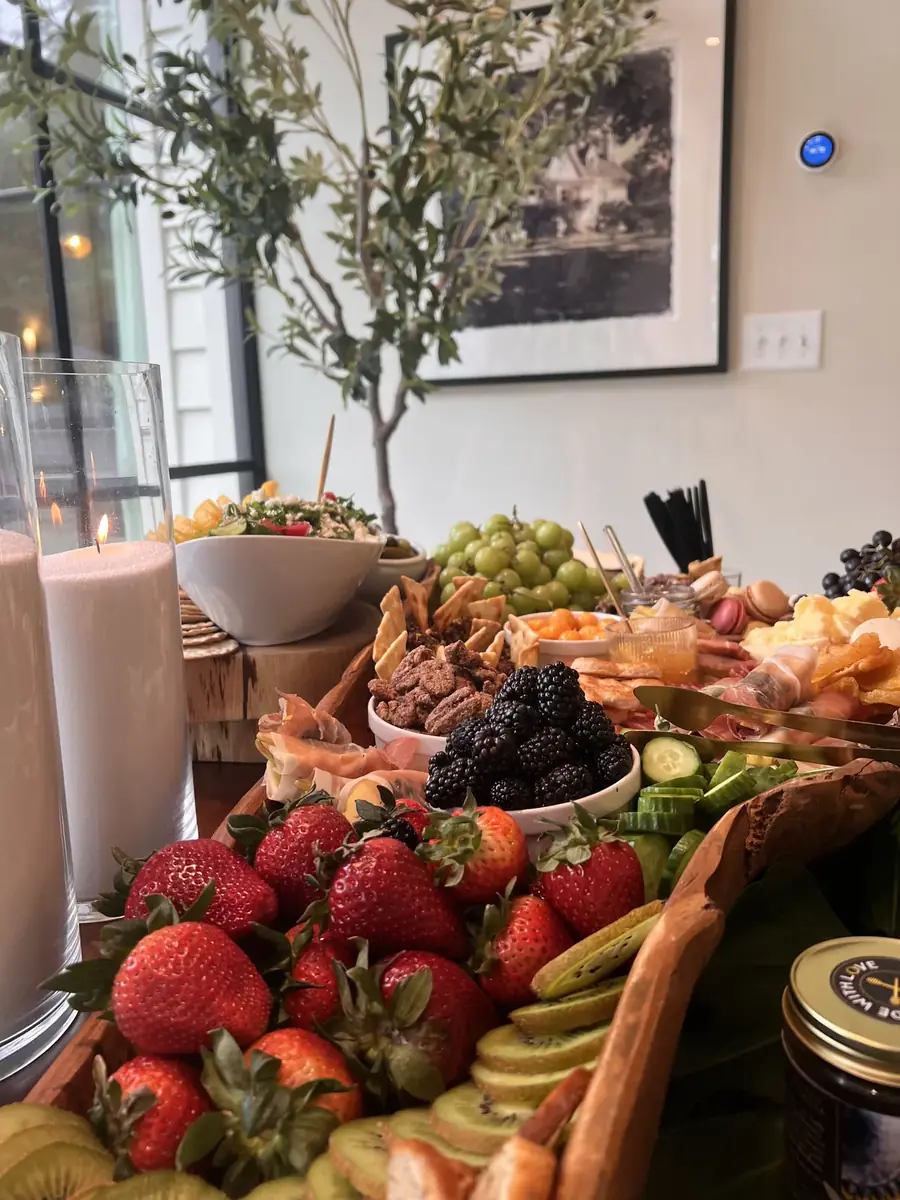 Grazing table with strawberries, breads and greenery beside tall windows